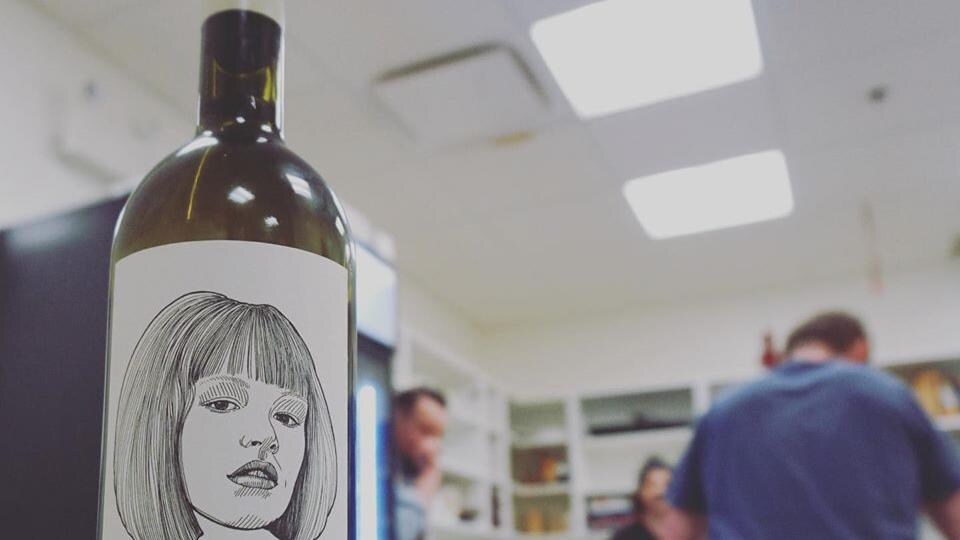 Une bouteille de vin en avant plan, une équipe de cuisinier qui discutent en arrière plan.