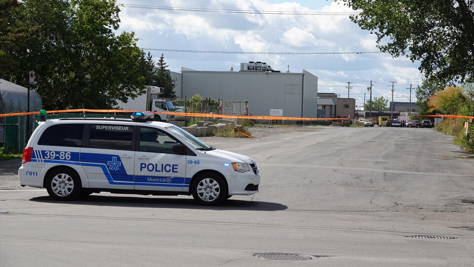 Un véhicule de police est garé à l'extérieur du périmètre de sécurité.