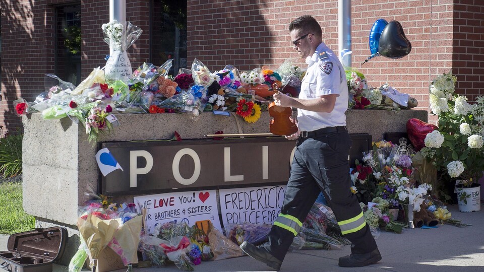 Un paramédic dépose le violon avec lequel il a joué un air en hommage aux policiers morts en service à Fredericton, dans un endroit où de nombreuses gerbes de fleurs ont été placées.