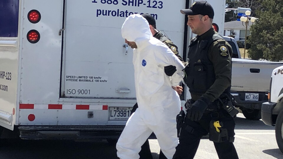 Un détenu en combinaison de plastique arrive au palais de justice escorté par deux policiers.