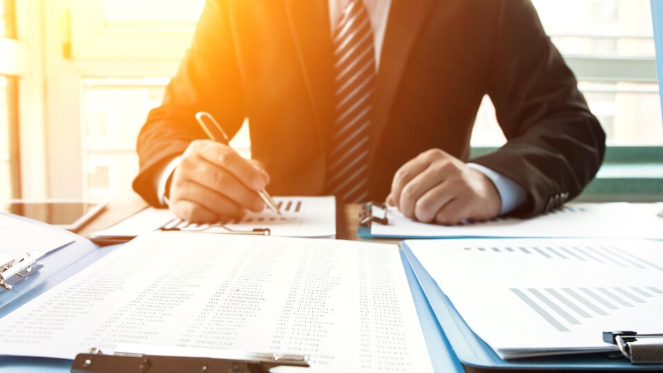 Un homme d'affaires travaille dans son bureau alors que le soleil se couche derrière lui.