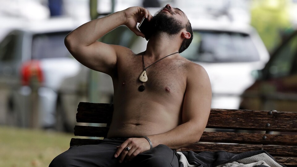 Un homme parle au téléphone mobile assis sur un banc de parc.