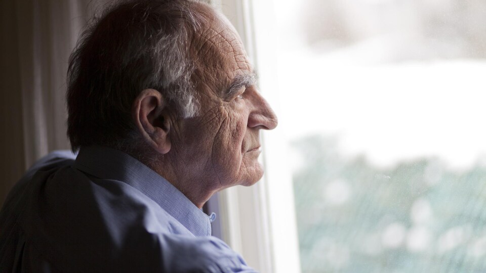 Un homme âgé regarde par la fenêtre.