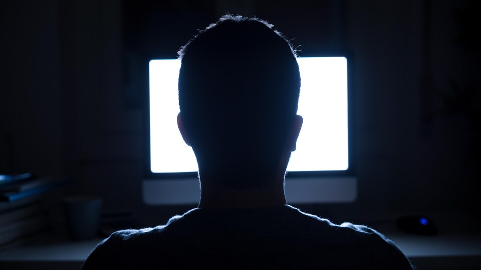Silhouette d'un homme devant la lumière d'un écran d'ordinateur dans la pénombre.