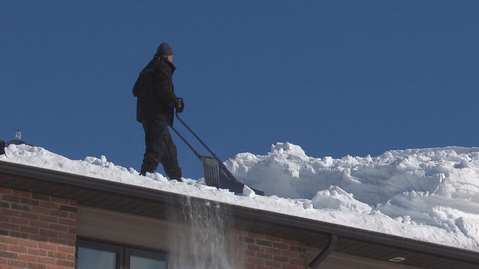 Un homme dégage une toiture de la neige qui s'y est accumulée