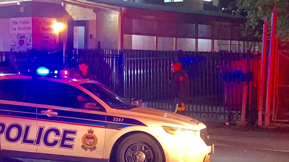 Une voiture de police aux gyrophares allumés est stationnée devant La Roulotte, l'édifice où est située la clinique d'injection supervisée du refuge de sans abri.