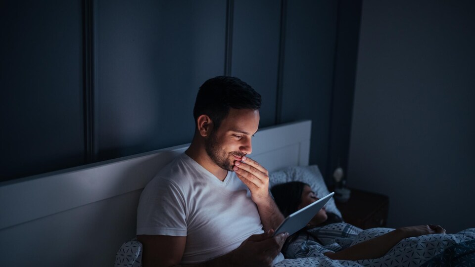 Un homme consulte sa tablette dans son lit.