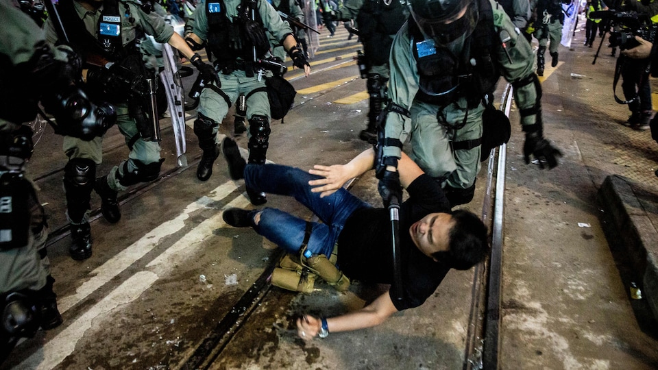 Un manifestant est renversé sur le sol par un policier armé d'une matraque.