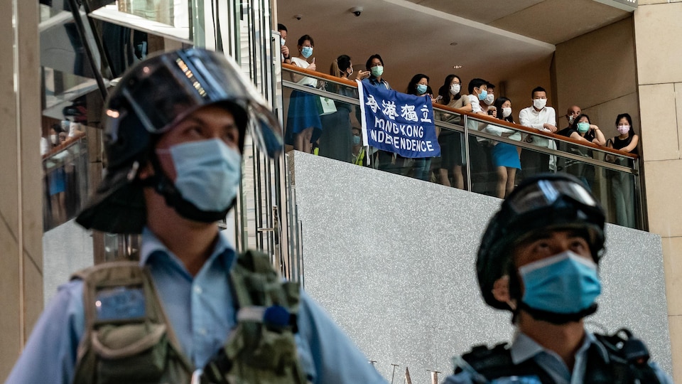 Des manifestants déploient une bannière disant « Indépendance de Hong Kong », vue entre deux agents de police.