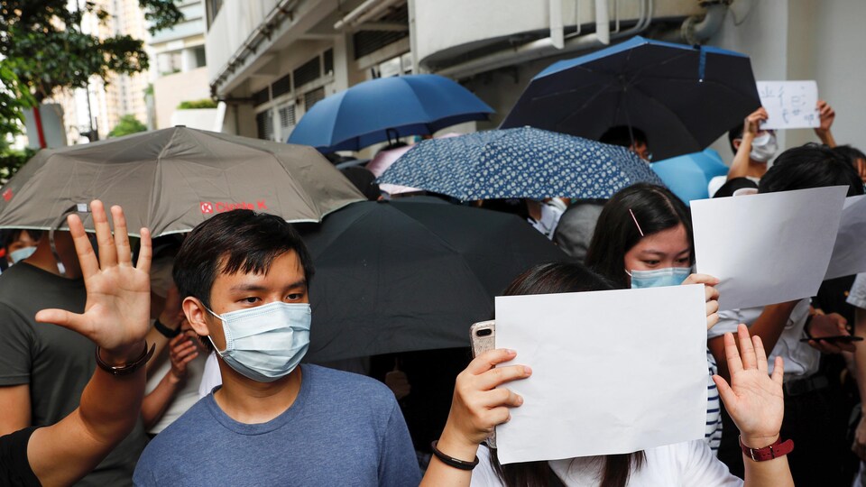 Plusieurs personnes réunies dans la rue, portant des masques, des pages blanches et des parapluies.