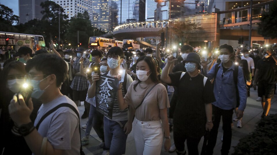 De jeunes adultes portant des masques de protection manifestent calmement en soirée dans une rue de la ville.