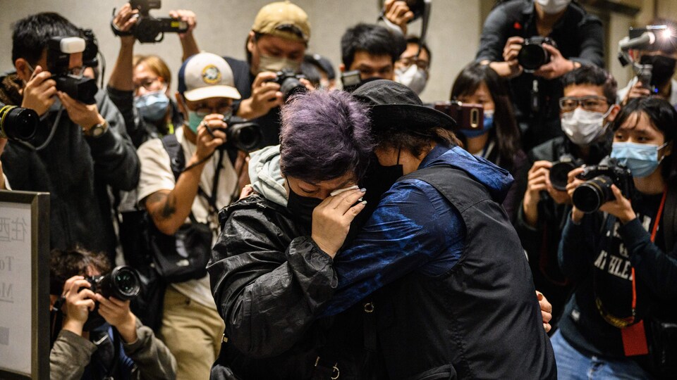 Deux personnes s'enlacent sous le regard de nombreux photographes.