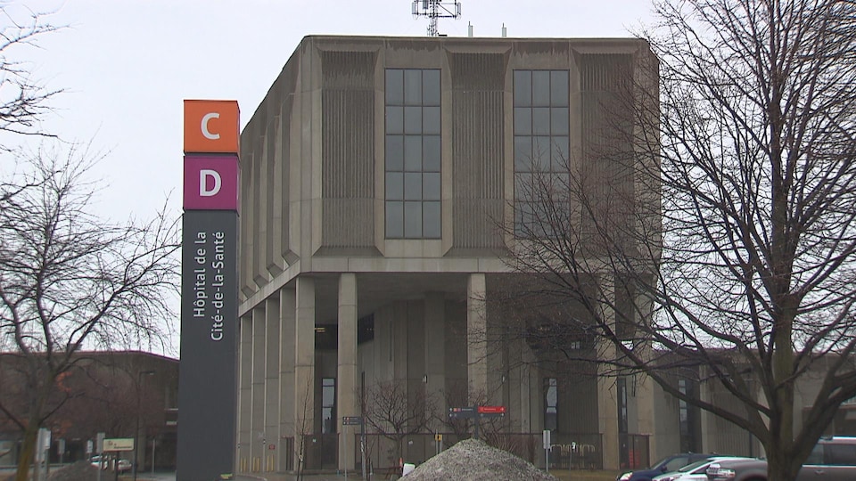 Un panneau portant le nom de l'hôpital à la verticale devant un bâtiment en béton par une journée pluvieuse de printemps.
