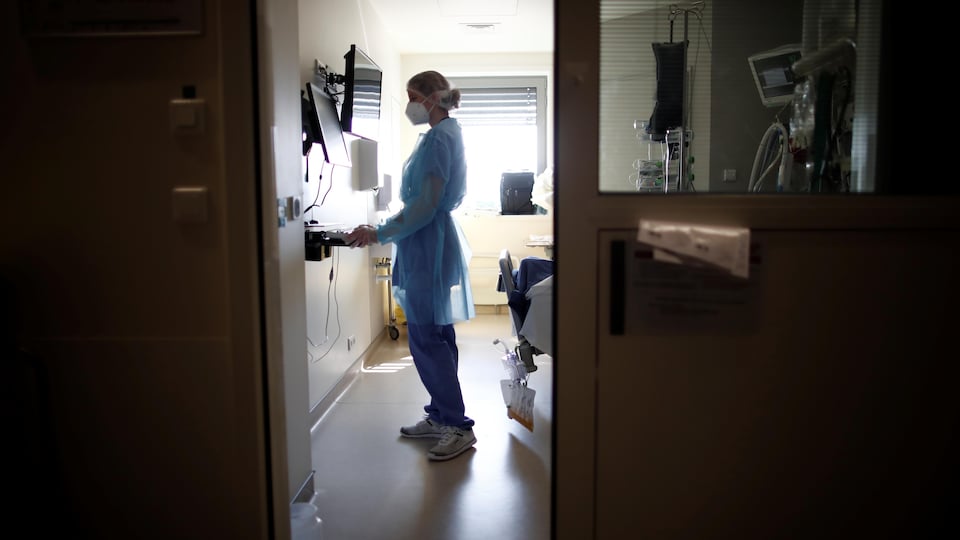 Une infirmière aperçue par la porte entrabâillée de l'unité des soins intensifs d'un hôpital.