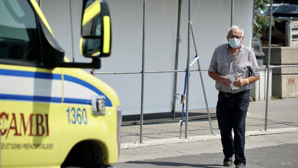 Un homme porte un masque de protection et se dirige vers une ambulance.