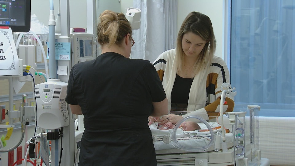 Une infirmière et une femme qui a accouché d'un bébé prématuré sont dans une chambre d'hôpital, debout autour de la couveuse.
