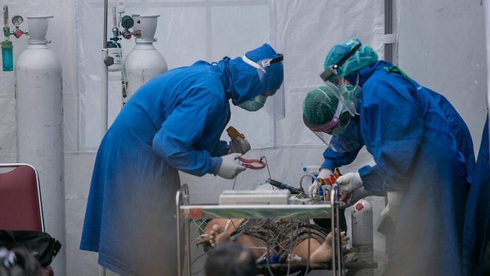 Trois soignants en combinaison bleue penchés au-dessus d'un patient alité.