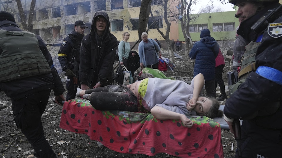 Une femme est évacuée sur une civière par des hommes au milieu de décombres.