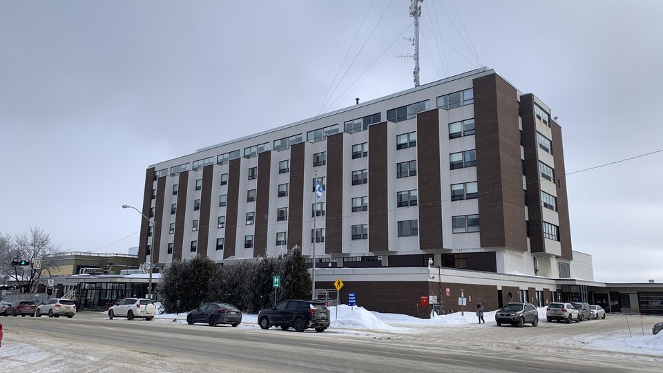 Des voitures sont stationnées devant l'hôpital et sur le côté de celui-ci.