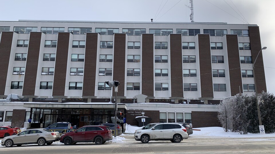 Plusieurs véhicules sont stationnés devant l'entrée principale de l'hôpital.