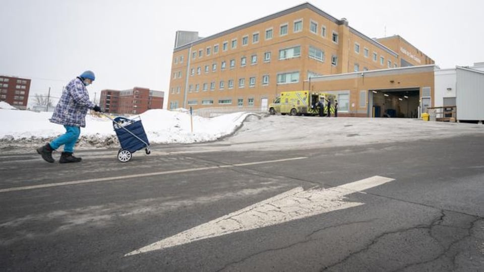 Une personne pousse un chariot à l'extérieur de l'hôpital de Saint-Eustache en hiver.