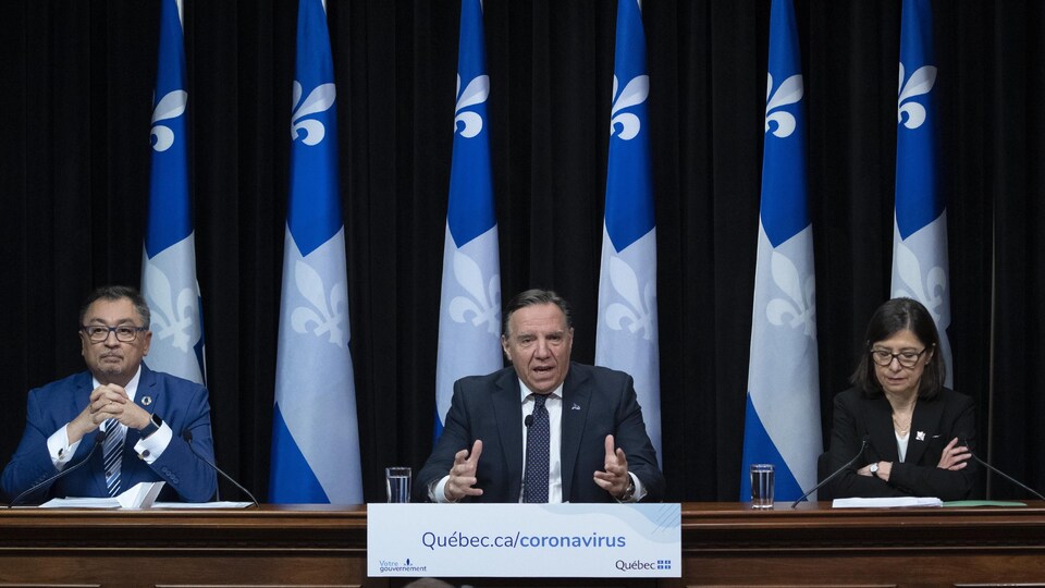 Trois personnes assises à une table devant des drapeaux du Québec.
