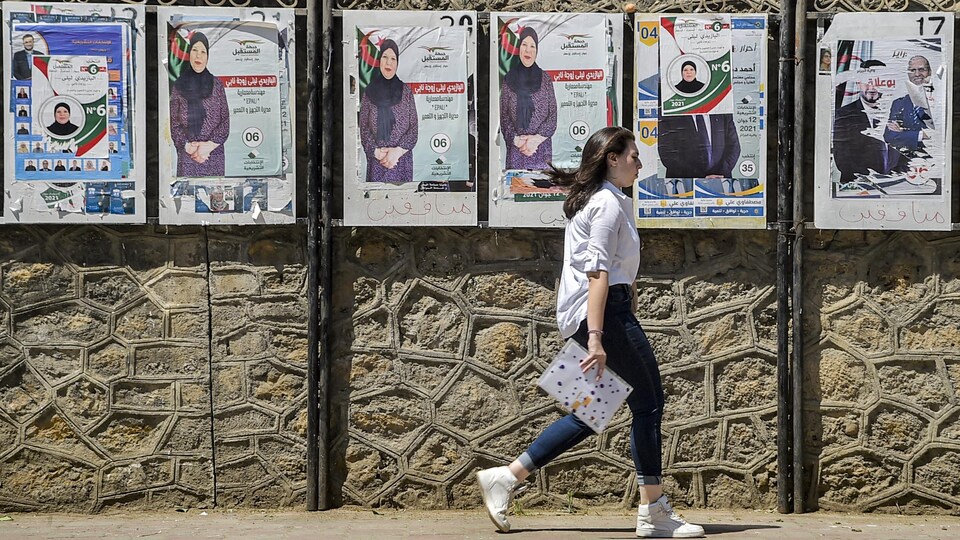 Une femme marche devant des affiches électorales.