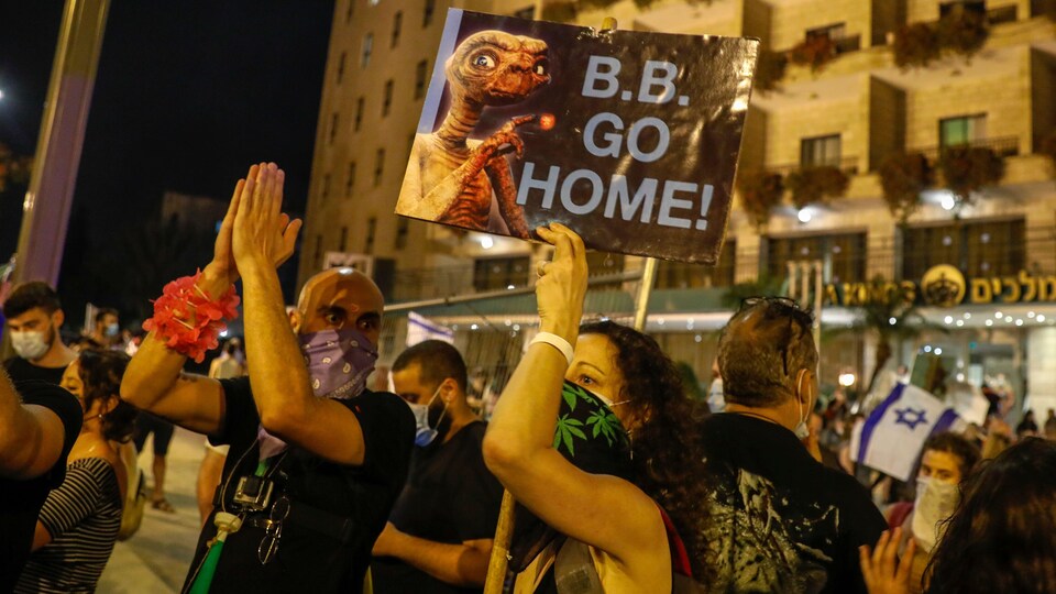 Une manifestante tient une pancarte sur laquelle on voir une photo de ET l'extraterrestre et sur laquelle est écrit «B.B. GO HOME».