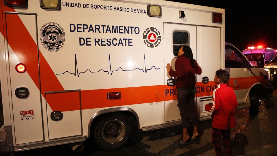 Une femme est appuyée sur une ambulance et un enfant se trouve derrière elle.