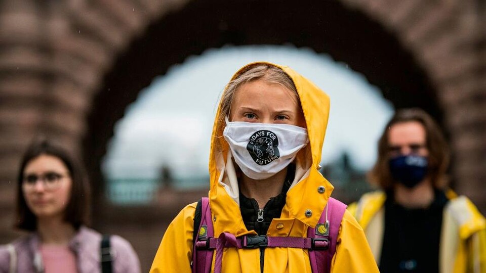 Vêtue d'un imperméable, Greta Thunberg fronce les sourcils. Elle porte un couvre-visage en tissu.