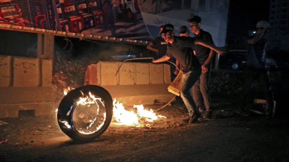De jeunes hommes autour d'un pneu enflammé, à la nuit tombée.