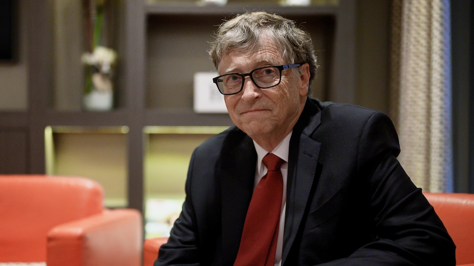 Bill Gates, assis sur un divan, regarde la caméra. 