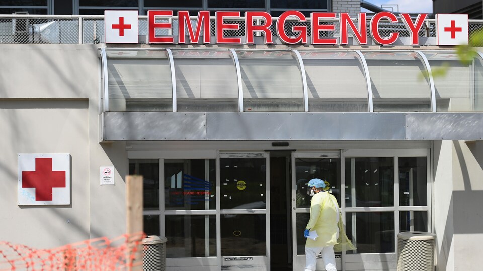Un homme masqué et vêtu d'une tenue de protection s'apprête à franchir la porte des urgences d'un hôpital.