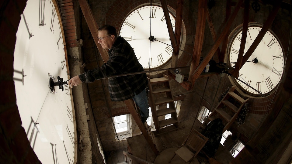 Plan large d'un homme qui remonte une des horloges d'une tour d'horloge.