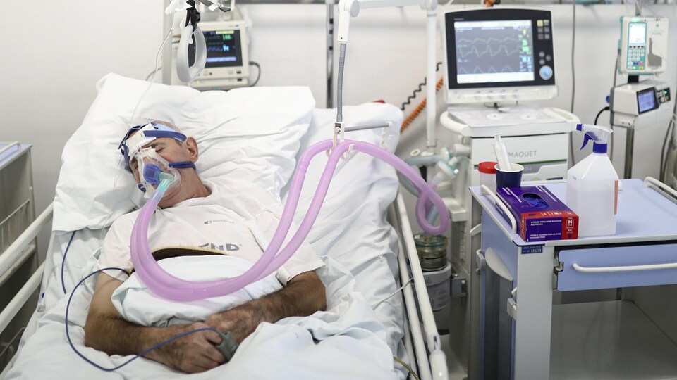 Un homme intubé couché dans un lit d'hôpital.