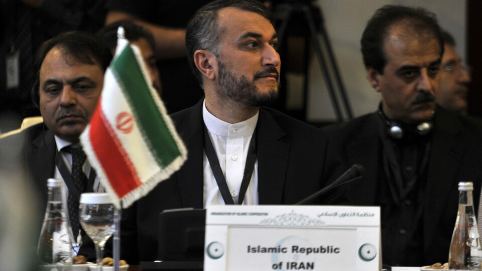 Hossein Amir-Abdollahian assis derrière un petit drapeau de l'Iran, entouré d'autres hommes.