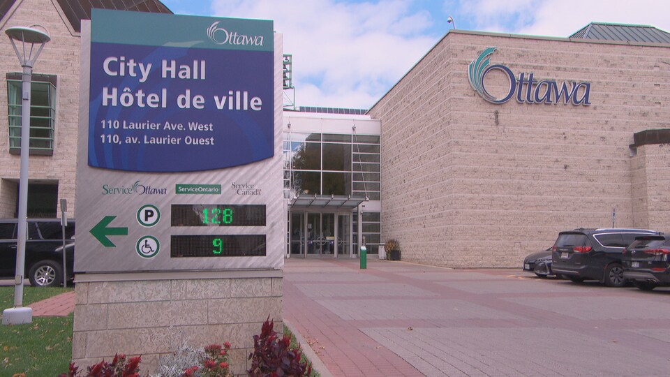 La façade de l'hôtel de ville d'Ottawa devant laquelle sont stationnés des voitures.