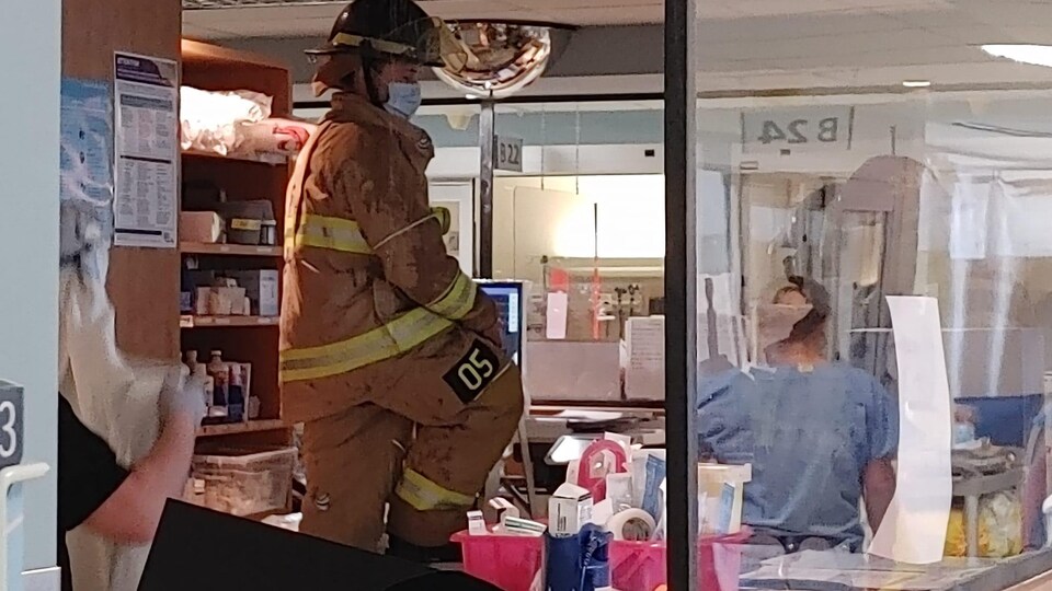 Un pompier se tient au milieu d'un bureau de l'hôpital. Le plafond est ouvert et de l'eau coule. 