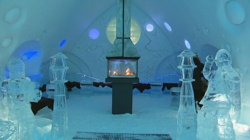 Un intérieur entièrement sculpté dans de la glace. Au milieu de la pièce, on aperçoit un poêle à l'intérieur duquel crépitent des flammes.