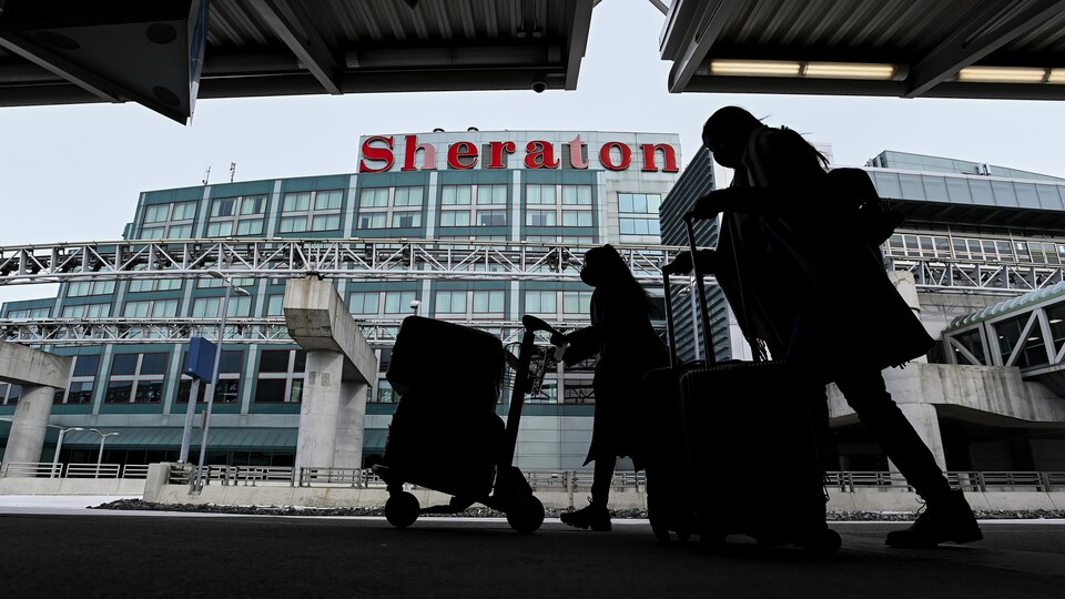Des voyageurs portent leurs valises devant un hôtel Sheraton à l'aéroport de Toronto.