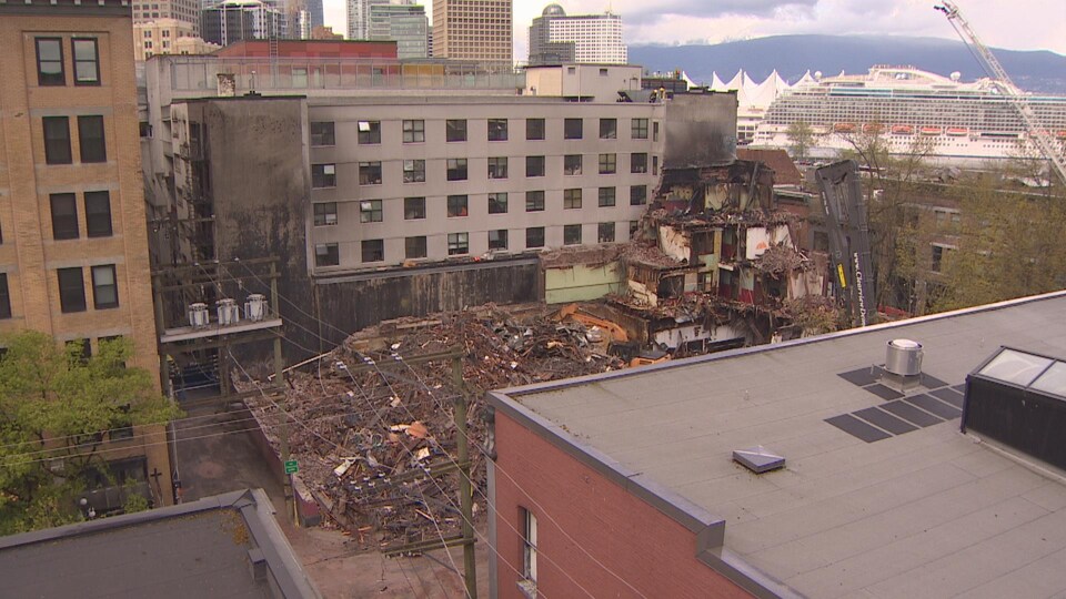 The ruins of one building lie on the ground mixed between two other buildings and in the distance you will see mountains and clouds, in Vancouver, in April 2022.