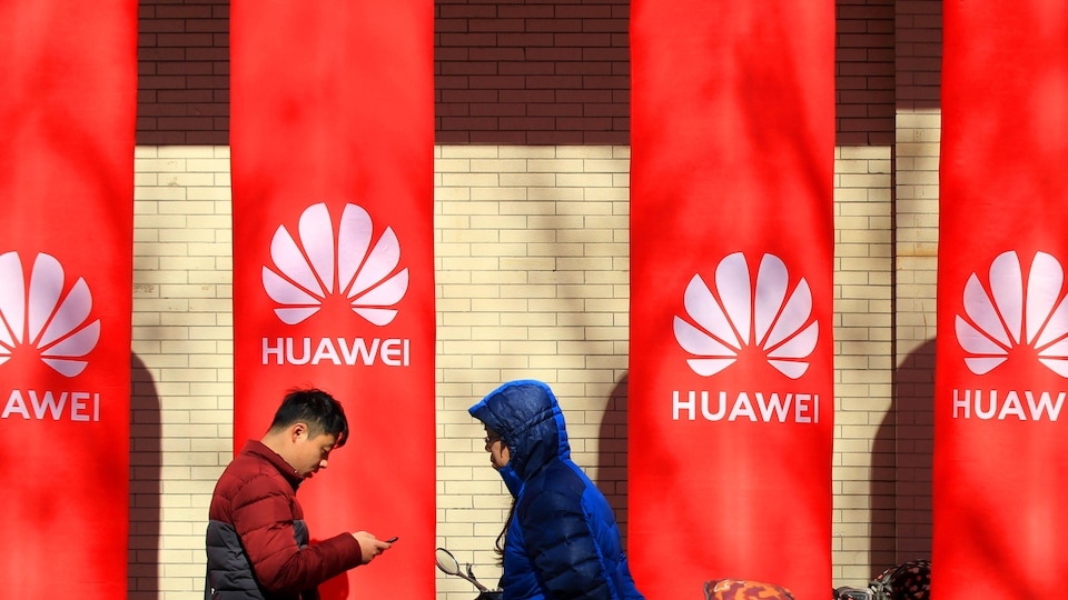 Des gens marchent à côté de poteaux ornés du logo de Huawei. 