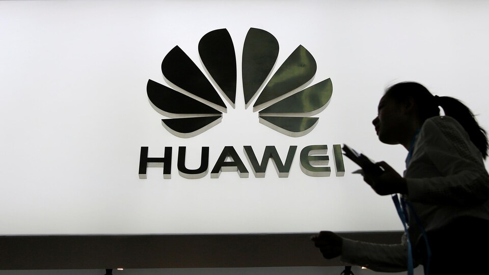 Des personnes marchent devant un panneau lumineux montrant le logo de Huawei.