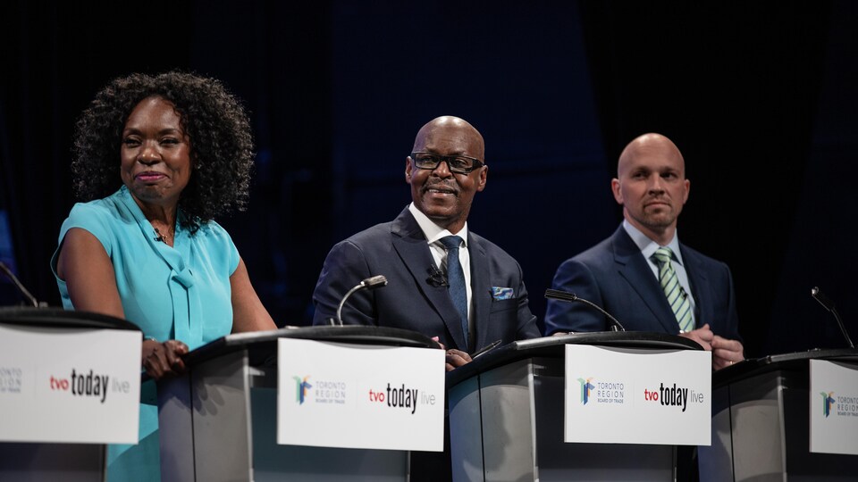 Gros plan sur les candidats Mitzie Hunter, Mark Saunders et Brad Bradford sur scène.
