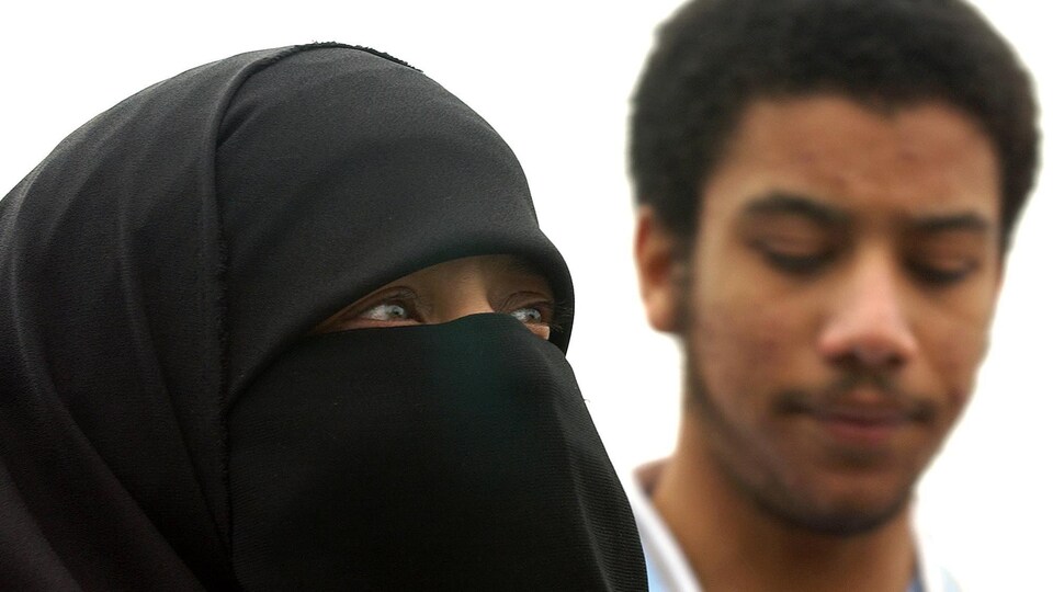 Une femme portant le niqab et un jeune homme en arrière-plan.