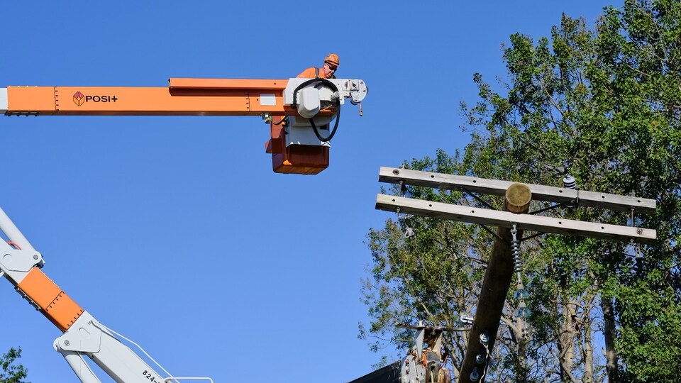 Un homme dans une nacelle dirige l'installation d'un poteau électrique.