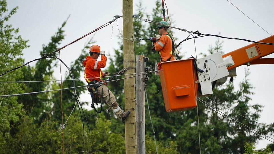 Deux travailleurs d'Hydro-Québec réparent un poteau électrique.