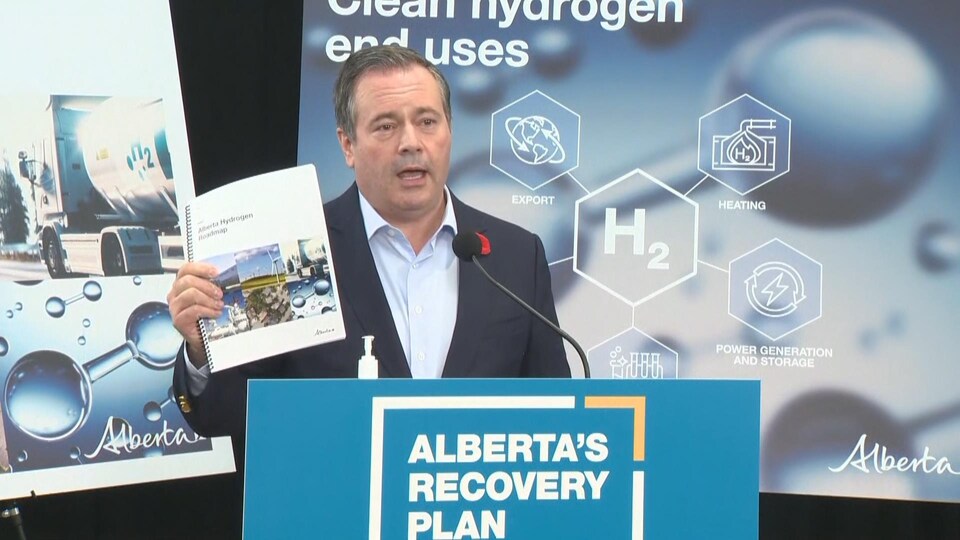 Jason Kenney à un podium, le document à la main.