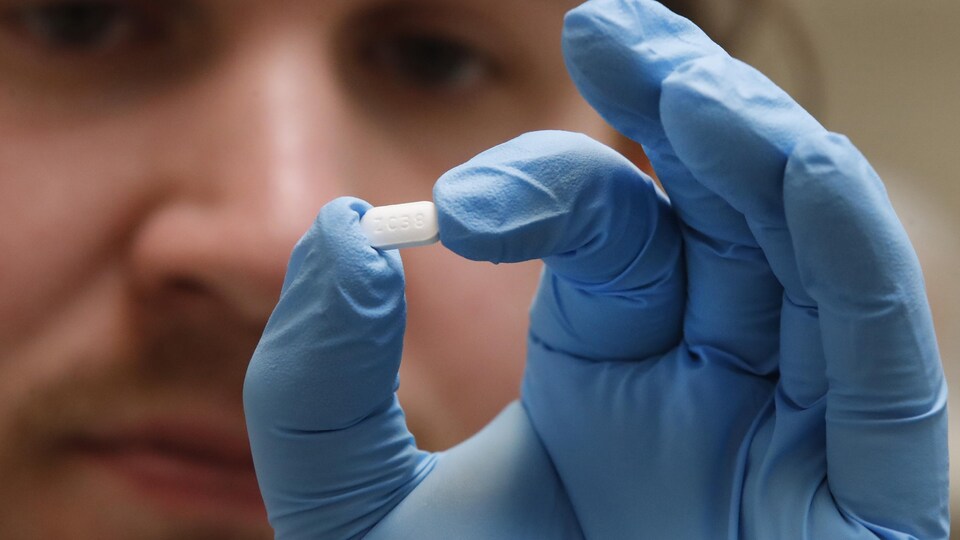 Un homme avec des gants chirurgicaux tient un comprimé d'hydroxychloroquine entre ses doigts. 