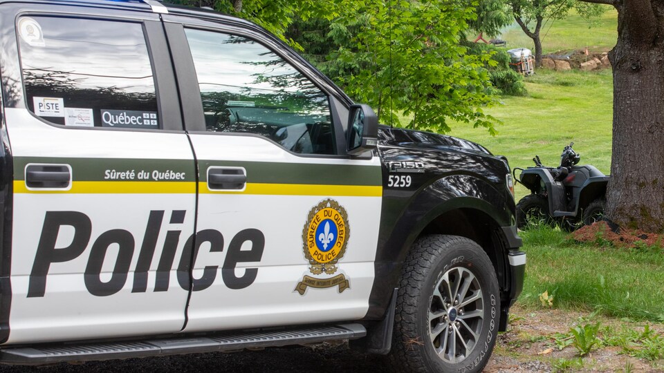 Un véhicule de la Sûreté du Québec et le VTT accidenté près d'un arbre.